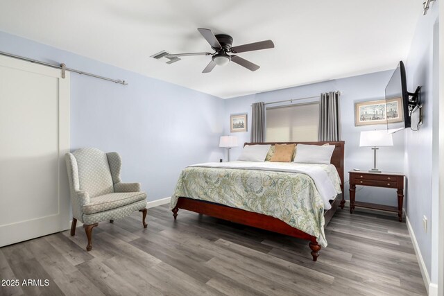 bedroom featuring hardwood / wood-style flooring, ceiling fan, and a barn door