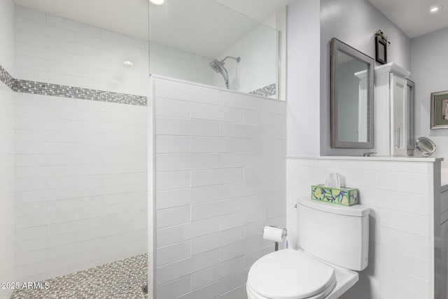 bathroom with a tile shower, vanity, tile walls, and toilet