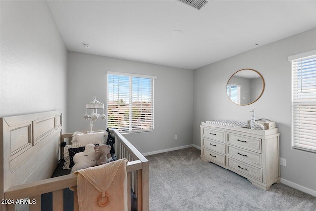 bedroom with multiple windows, light colored carpet, and a crib