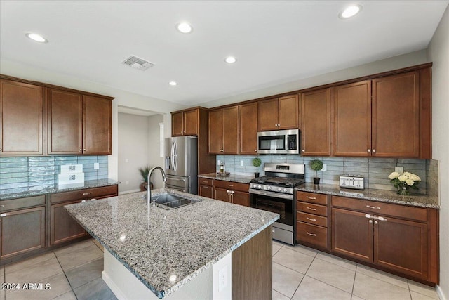 kitchen featuring light stone counters, stainless steel appliances, sink, light tile patterned floors, and a center island with sink