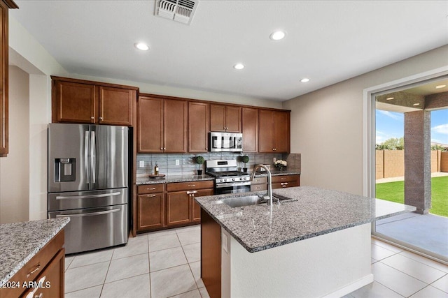 kitchen featuring a kitchen island with sink, sink, light tile patterned floors, light stone countertops, and stainless steel appliances