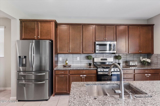 kitchen featuring light stone countertops, appliances with stainless steel finishes, decorative backsplash, sink, and light tile patterned floors