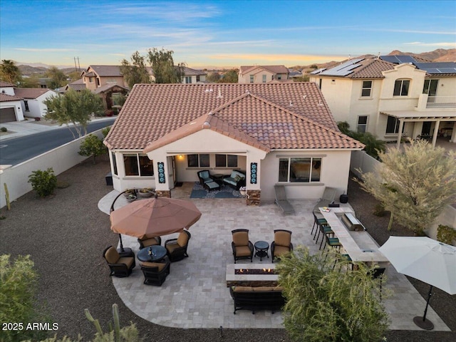 rear view of property with a fenced backyard, a tiled roof, stucco siding, a patio area, and an outdoor living space with a fire pit