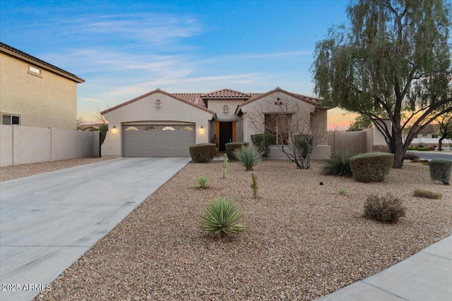 mediterranean / spanish-style house with a garage, concrete driveway, fence, and stucco siding