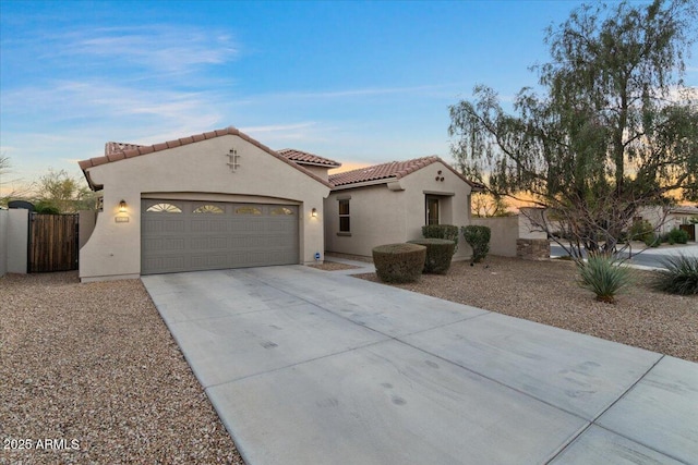 mediterranean / spanish-style house with concrete driveway, a tile roof, an attached garage, fence, and stucco siding