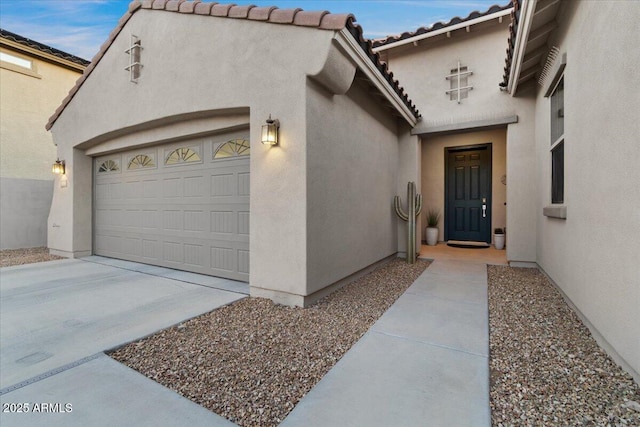 property entrance featuring concrete driveway, an attached garage, a tile roof, and stucco siding