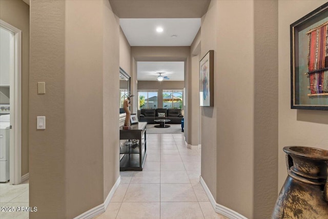 hall featuring washer / clothes dryer, light tile patterned flooring, and baseboards