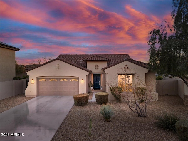 mediterranean / spanish-style home with concrete driveway, an attached garage, fence, and stucco siding