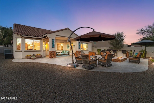 back of house at dusk with a patio, fence, a tiled roof, stucco siding, and an outdoor living space with a fire pit