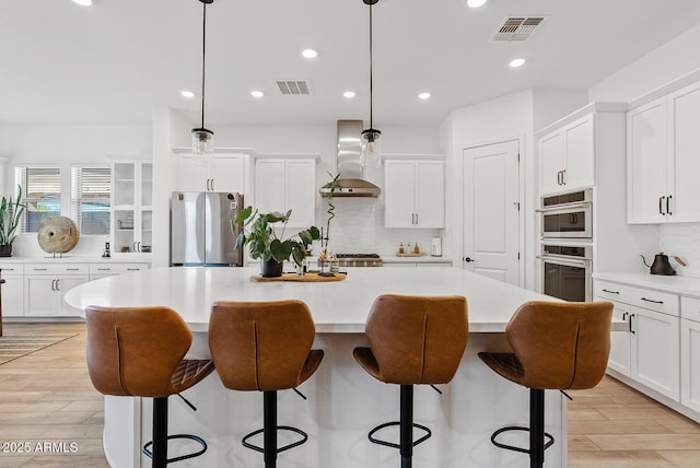 kitchen featuring freestanding refrigerator, wall chimney exhaust hood, a kitchen island, tasteful backsplash, and a breakfast bar