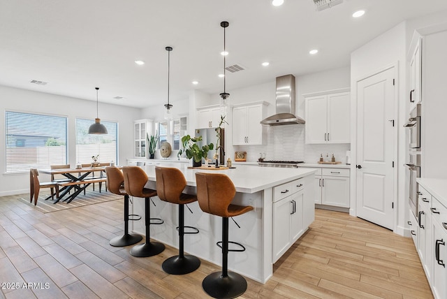 kitchen with wall chimney exhaust hood, light wood-style flooring, backsplash, light countertops, and recessed lighting