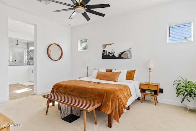 bedroom featuring light colored carpet, baseboards, ceiling fan, and ensuite bathroom
