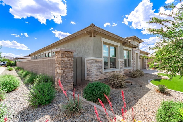 view of home's exterior with stone siding, stucco siding, fence, an attached garage, and driveway