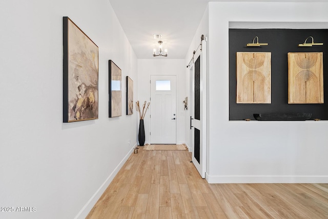 hallway with a chandelier, light wood-style flooring, a barn door, and baseboards