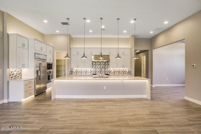 kitchen featuring white cabinets, light countertops, decorative backsplash, built in appliances, and wood tiled floor