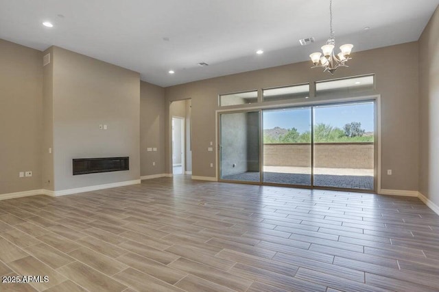 unfurnished living room with baseboards, visible vents, wood finish floors, an inviting chandelier, and a glass covered fireplace