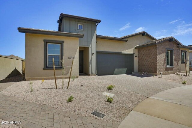 view of front of home with stucco siding, decorative driveway, board and batten siding, a garage, and brick siding