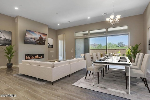 living area featuring baseboards, visible vents, wood finish floors, an inviting chandelier, and a glass covered fireplace