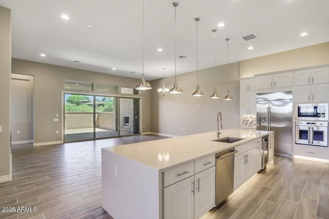 kitchen with wood finish floors, visible vents, built in appliances, and a sink