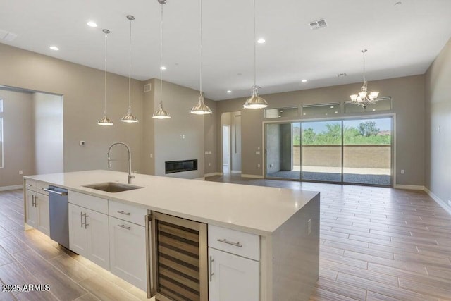 kitchen featuring a kitchen island with sink, a sink, wine cooler, open floor plan, and stainless steel dishwasher