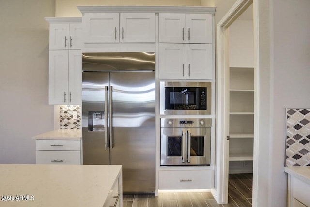 kitchen with tasteful backsplash, white cabinets, stainless steel appliances, and wood finish floors