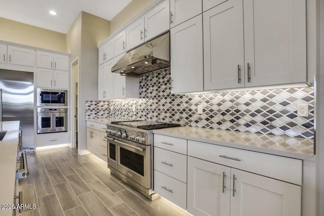 kitchen featuring under cabinet range hood, tasteful backsplash, white cabinets, light countertops, and built in appliances