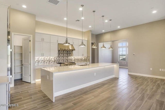 kitchen with visible vents, wood finish floors, light countertops, under cabinet range hood, and tasteful backsplash