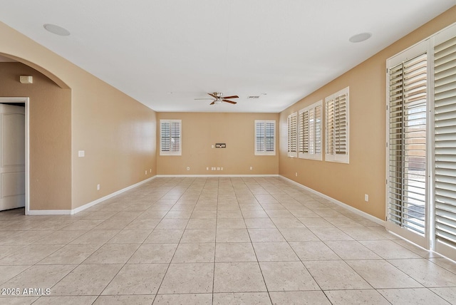 unfurnished room with a ceiling fan, arched walkways, baseboards, and light tile patterned floors