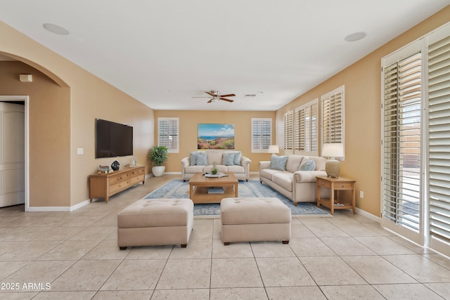 living area with arched walkways, ceiling fan, baseboards, and light tile patterned floors