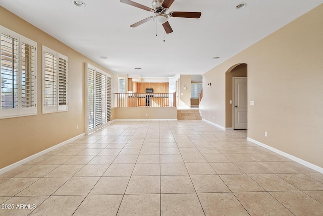 empty room featuring light tile patterned floors, baseboards, arched walkways, and a ceiling fan