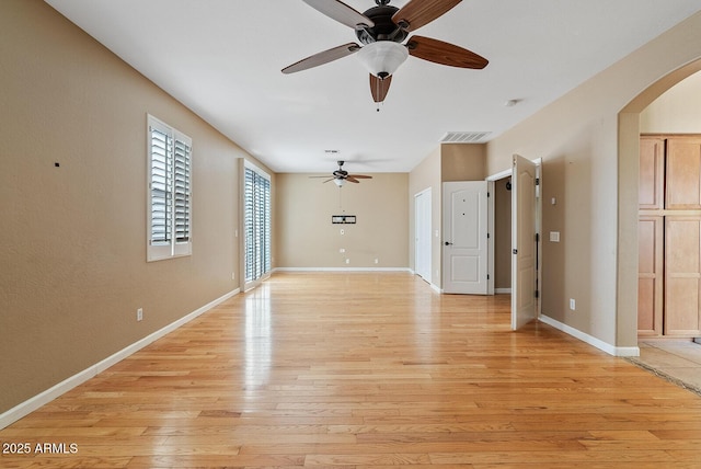 unfurnished living room featuring arched walkways, ceiling fan, light wood-style flooring, visible vents, and baseboards