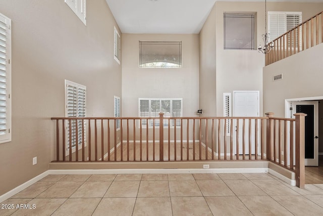 corridor featuring a high ceiling, tile patterned flooring, visible vents, and baseboards