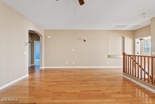 spare room featuring light wood-type flooring, visible vents, ceiling fan, and arched walkways