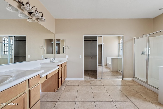 bathroom featuring a walk in closet, double vanity, a stall shower, baseboards, and tile patterned floors