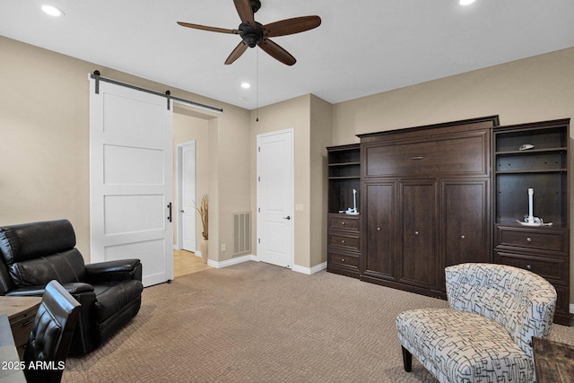 sitting room featuring light carpet, a barn door, and ceiling fan