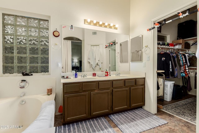 full bathroom with a sink, double vanity, a bath, tile patterned flooring, and a walk in closet