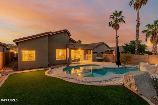 pool at dusk with a fenced backyard, a yard, a hot tub, a fenced in pool, and a patio area