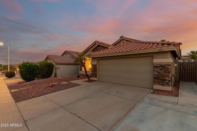 view of front of house with stucco siding, a tiled roof, driveway, stone siding, and an attached garage