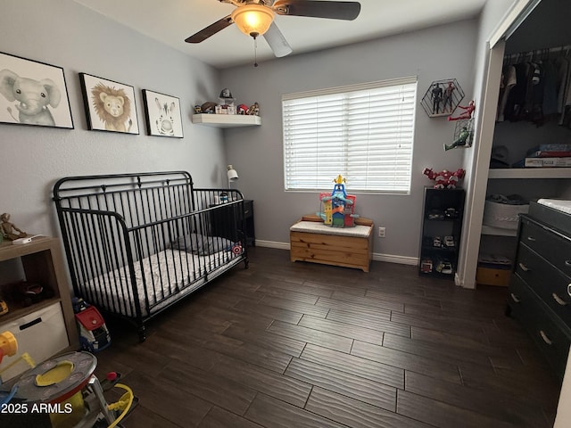 bedroom with dark wood-style floors, a closet, ceiling fan, a nursery area, and baseboards