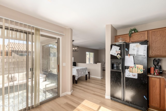 kitchen featuring black fridge with ice dispenser, an inviting chandelier, hanging light fixtures, and light hardwood / wood-style floors