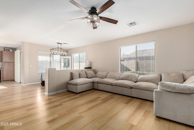 living room featuring a healthy amount of sunlight, ceiling fan with notable chandelier, and light wood-type flooring