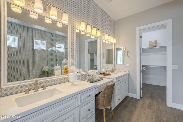 bathroom with a spacious closet, baseboards, a tile shower, wood finished floors, and vanity