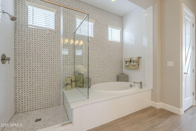 full bathroom featuring a bath, a stall shower, baseboards, and wood finished floors