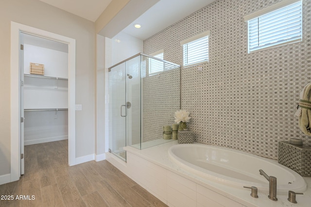 bathroom featuring a walk in closet, a garden tub, a stall shower, wood finished floors, and baseboards