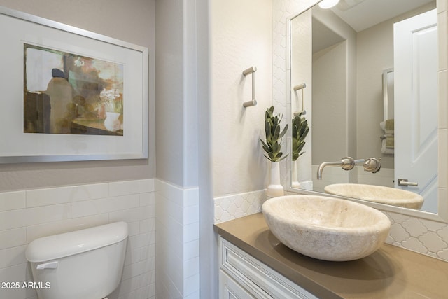 half bathroom with toilet, vanity, and tile walls