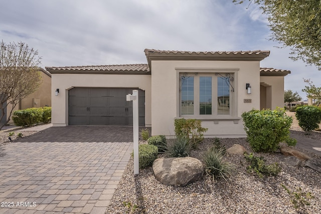 mediterranean / spanish home with stucco siding, decorative driveway, an attached garage, and a tile roof