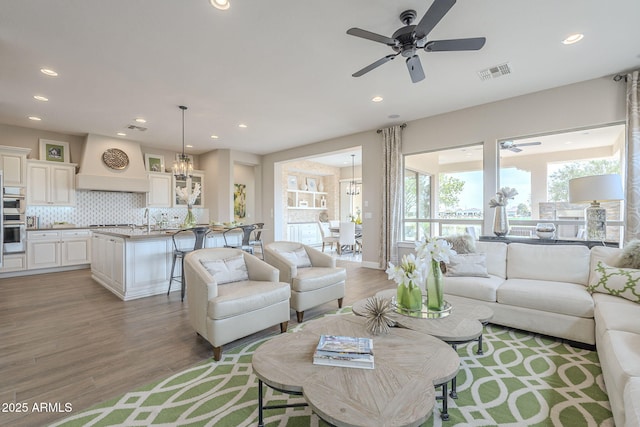 living area with ceiling fan with notable chandelier, recessed lighting, visible vents, and light wood-type flooring