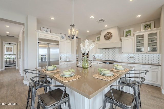 kitchen with custom exhaust hood, white cabinets, visible vents, and stainless steel built in fridge