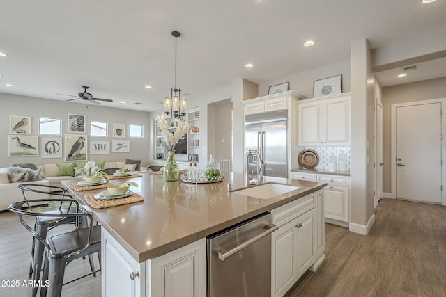 kitchen featuring wood finished floors, an island with sink, a sink, appliances with stainless steel finishes, and open floor plan