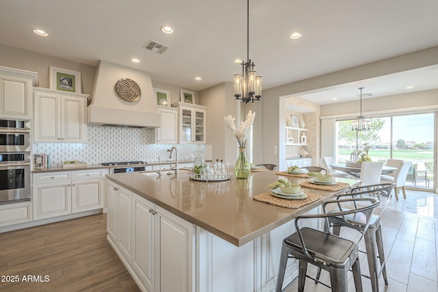 kitchen with visible vents, backsplash, custom exhaust hood, white cabinets, and a sink